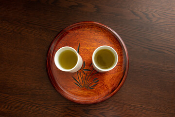 木製の丸いお盆と白いコップに入った緑茶
