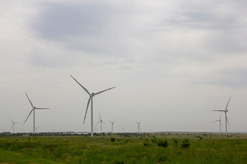 Industrial wind turbines are on the plain. Huge windmills stand on the plain under a gloomy sky.