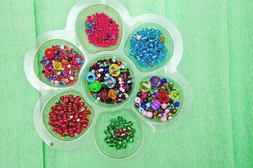 multicolored beads, beads for needlework, background with beads, close-up, colorful beads in a box on a green background.