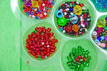 multicolored beads, beads for needlework, background with beads, close-up, colorful beads in a box on a green background.