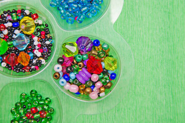 multicolored beads, beads for needlework, background with beads, close-up, colorful beads in a box on a green background.
