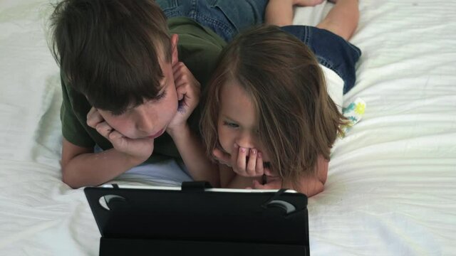 Children watching tablet while lying on the bed.