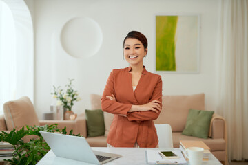 Smiling woman with arms crossed stands at her workplace in home office