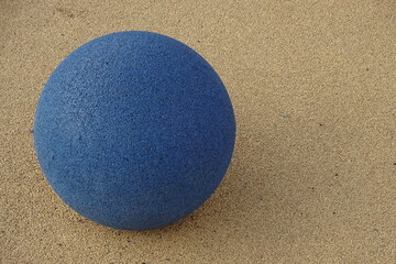 Close up of a dark blue color stone ball on the left downside on yellow asphalt grain textured background. Reidi tee street, Tallinn, Estonia. June 2021