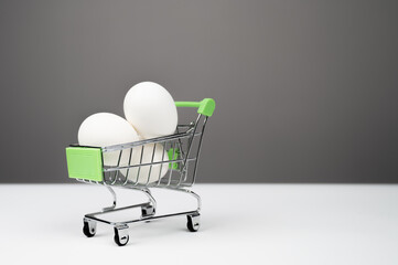 Fresh chicken white eggs in a shopping trolley over gray background