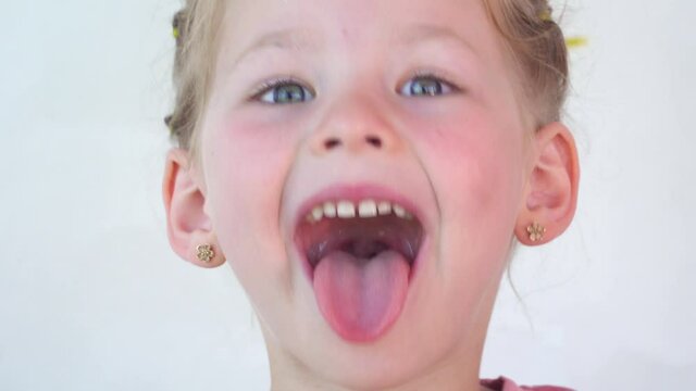 little girl show tongue, throat. portrait with wide open mouth and protruding tongue. with clear view pulls out long tongue. soft palate and mouth to dentist. mouth is wide open, tongue is stuck out.