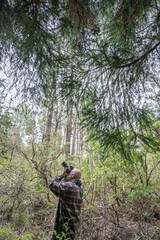 Male senior with a camera enjoying hobby photography outdoors while hiking in a forest