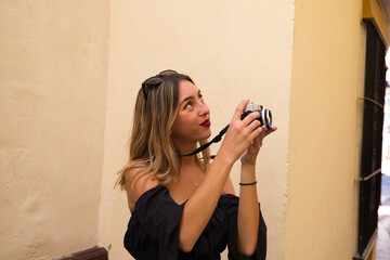 Fototapeta premium Beautiful young woman on holiday. She is taking a photo of a monument in the street. The woman is happy about the city she is visiting. Holiday concept, traveling.