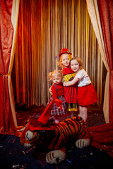 Small girls during a stylized theatrical circus photo shoot in a beautiful red location. Young models posing on stage with curtain. Sisters or female friends together