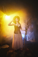 Young slim woman looking like witch having fun on Halloween in a dark room with yellow light and smoke. Carnival concept and Halloween party