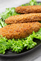 Southern fried chicken breast with spicy breadcrumbs on a bed of Lollo Biondo lettuce. On a black plate with a grey wood background