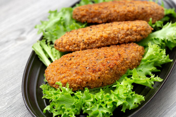 Southern fried chicken breast with spicy breadcrumbs on a bed of Lollo Biondo lettuce. On a black plate with a grey wood background