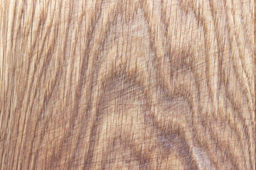 An oak kitchen chopping board covered in knife scratches. Uneven texture of a polished board with a pattern and streaks of natural wood.