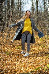 a woman in a coat and cropped trousers with a black and white print, a yellow sweater and a hat, walks in an autumn park along yellow, fallen leaves. oberations, blur. shot with an old lens