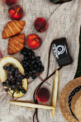 Photo of peaches, melon, grapes, straw hat abs retro camera on linen rug. Picnic snapshot with fruits.