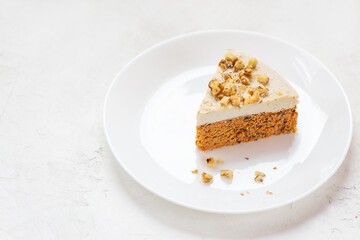 Slice of carrot cake with coconut cream and walnuts on a white plate. Raw dessert, no baked goods. Sugar, gluten and lactose free.