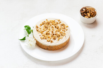 Carrot cake with coconut cream and walnuts on a white plate. Raw dessert, no baking. Sugar, gluten and lactose free.