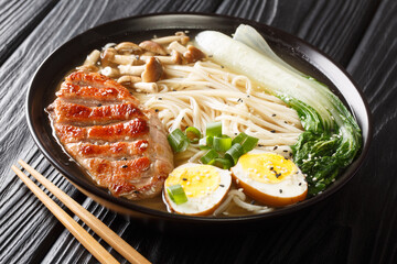 Asian ramen noodle soup with with duck, mushrooms, eggs and pak choi cabbage in bowl on black table close up. horizontal