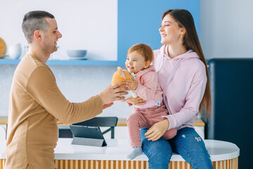 Smiling young couple with their adorable baby daughter playing together in living room at home