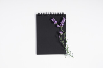 Black notebook cover and sprig of lavender on white background. Flat lay, top view, copy space