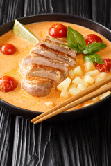 Thai red curry duck with pineapple, tomatoes and basil closeup in the plate on the black table. Vertical