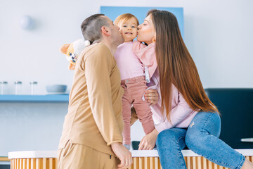 Happy family of three. Cheerful parents kiss their cute little daughter in the kitchen.