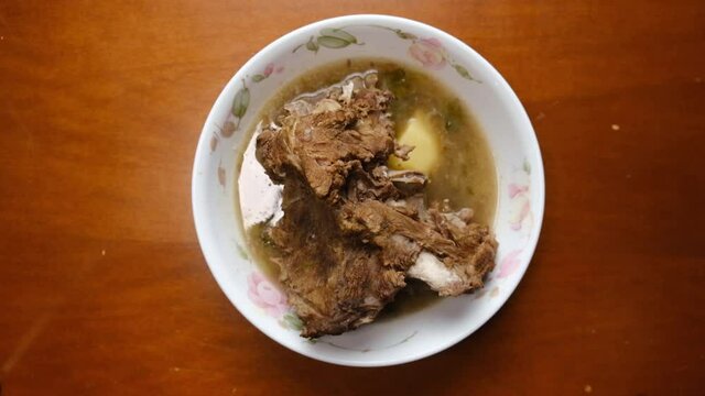 Low exposure with noise effect added footage bowl of homemade "sup tulang" been put on the table. Is an aromatic beef soup flavoured with spices like coriander, cinnamon, chilli, onions and aniseed.