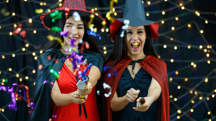 Cheerful girlfriends with serpentine crackers celebrating Halloween