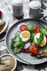 Gray plate with egg, arugula and tomato sandwich on a colorful graphic table (Asian, southern style). A healthy breakfast with vegetables and herbs.