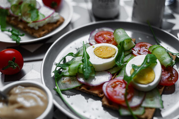Gray plate with egg, arugula and tomato sandwich on a colorful graphic table (Asian, southern style). A healthy breakfast with vegetables and herbs.