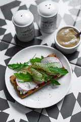 A gray plate with a sandwich with buko cheese, radish and oruguts on a colorful graphic table (Asian, southern style). A healthy breakfast with vegetables and herbs.