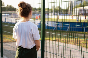 A girl stands and looks through the fence at the athletes playing at the stadium. The girl imagines...
