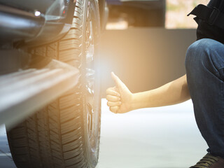 Man hand thumb up near big wheel of new car with light flare