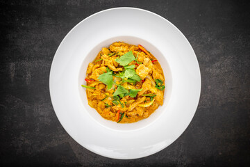 Gai Pad Pong Karee, Thai food, Stir Fried Chicken with Curry Powder in simple white ceramic plate on dark tone texture background, top view
