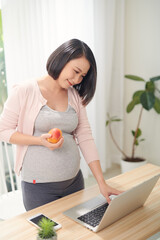 Beautiful pregnant business woman is writing in her notebook and smiling while  working place at home