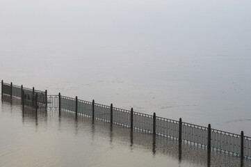 The fence of the city embankment during flooding with water and fog. Geometrically straight line. Summer colorless early morning before sunrise.