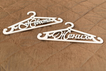 Groom and bride white hanger on brown background. Wedding attributes, symbol. Close-up. Wedding morning of the bride and groom. Hanger with the inscription "bride and groom"