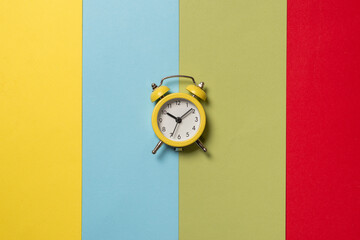Yellow alarm clock on a yellow, blue, red and green background. Time concept.