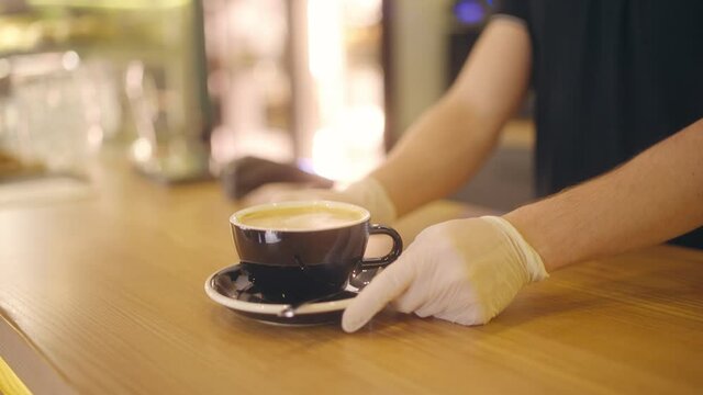 Barista in gloves serving cup of coffee to customer in cafe pandemic precautions