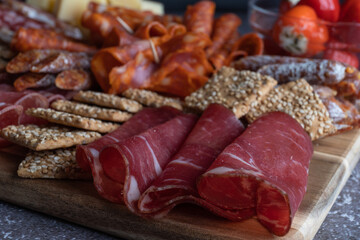 Cutting board with ham, salami, cheese and crackers on a dark stone background.