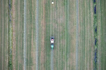 Agricultural tractor collects mowed grass for agricultural use and wraps hay bales in a plastic...