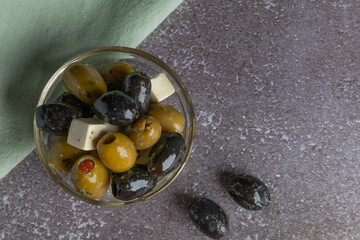 delicious Italian appetizer, green and black olives with cheese cubes and herbs in the olive oil