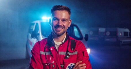 Portrait of Caucasian happy young male paramedic in red uniform smiling to camera and standing...