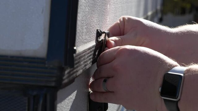 A close up of locking the tent trailer with the clasp on the side to secure it for travel. 