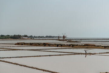 Saline of the Laguna Marsala,Sicily,Italy.Nature reserve with beautiful windmills,brine pools shimmering with different colors,traditional production method of sea salt.Salt flats in cloudy summer day