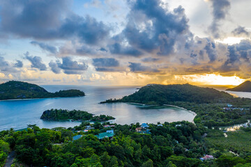 Mahe Island coast drone sunset landscape with dramatic sky, clouds, lush tropical forest and small islands around.