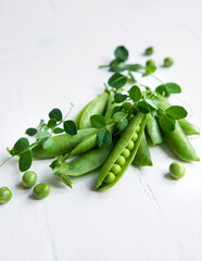 Fresh green peas pods and green peas with sprouts on white tile background.