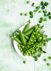 Fresh green peas pods and green peas with sprouts on green wooden background.