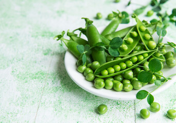 Fresh green peas pods and green peas with sprouts on green wooden background.