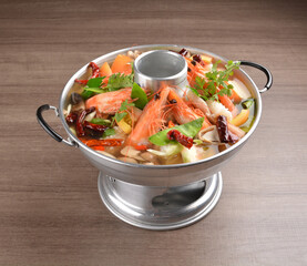 thai clear tom yum spicy chilli hot soup with seafood, meat and vegetables in hot pot in wood background asian halal menu